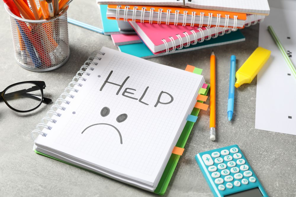 Open notebook on grey table with word “Help” with unhappy face