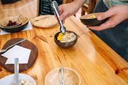 Chef preparing vegan breakfast with mango, banana, raspberries, cereals and muesli in coconut bowl