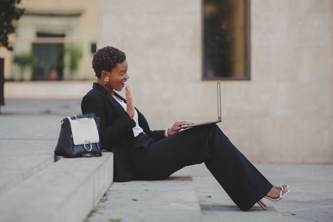 Stylish Black woman with laptop on steps near handbag