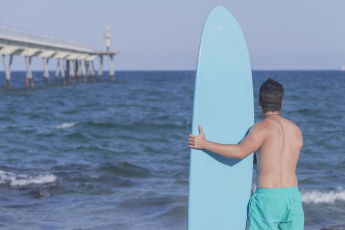 Male surfer holding his surfboard looking out to the sea