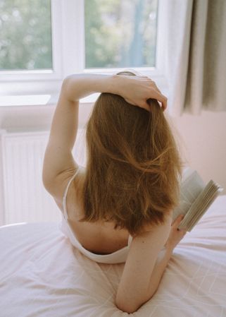 Back view of woman holding a book sitting on bed