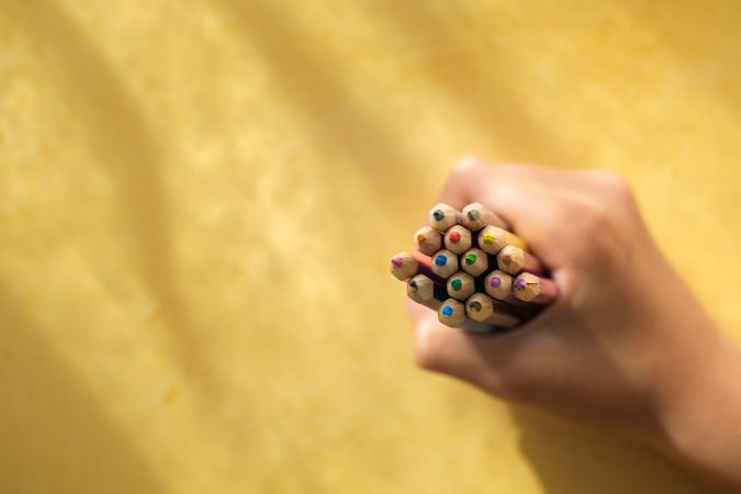 A child's hand picking up coloured pencils on a yellow backgroun