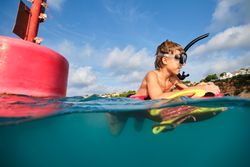 Happy kid in diving mask in seawater near red buoy