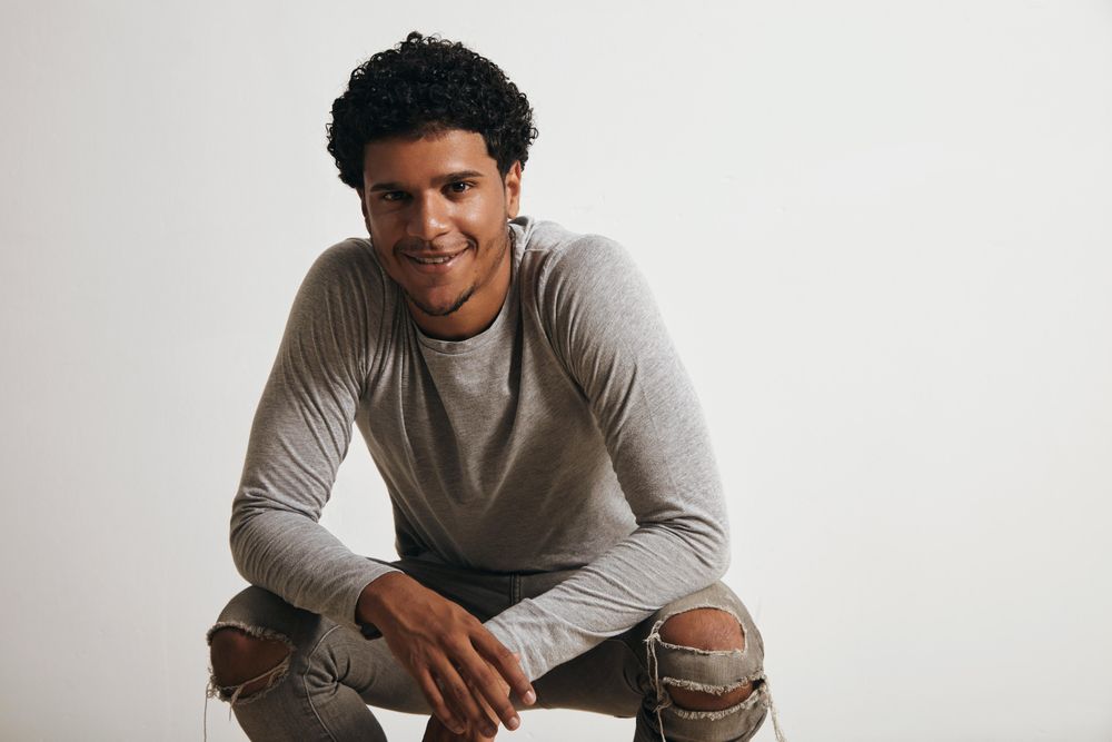 Smiling Black man crouching down wearing jeans and grey shirt