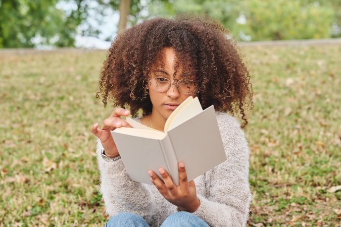 Black female flipping pages of book in nature