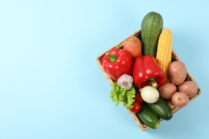 Wicker basket with vegetables on blue background, copy space