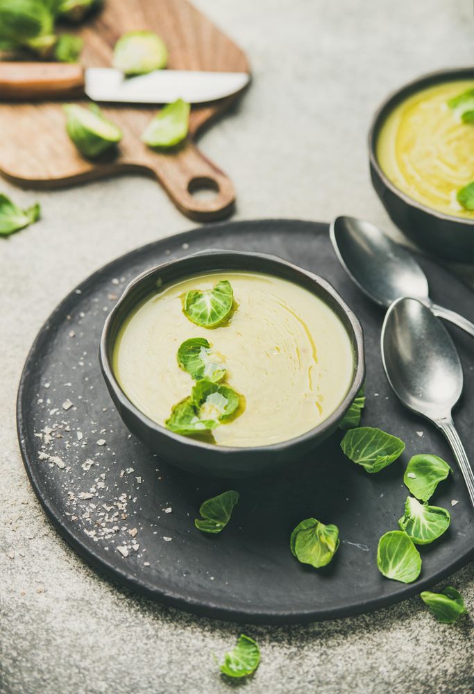 Bowls of Brussels sprout soup, on dark plate, garnished with fresh sprouts, vertical composition