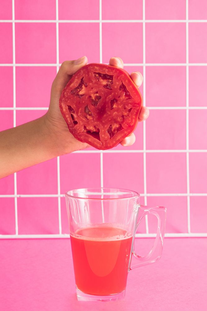 Hand holding half of red tomato and squeezing in glass
