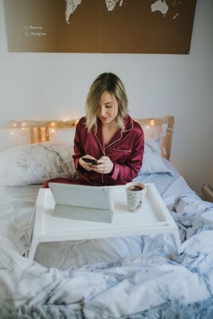 Woman sitting in bed with tablet and looking on smartphone