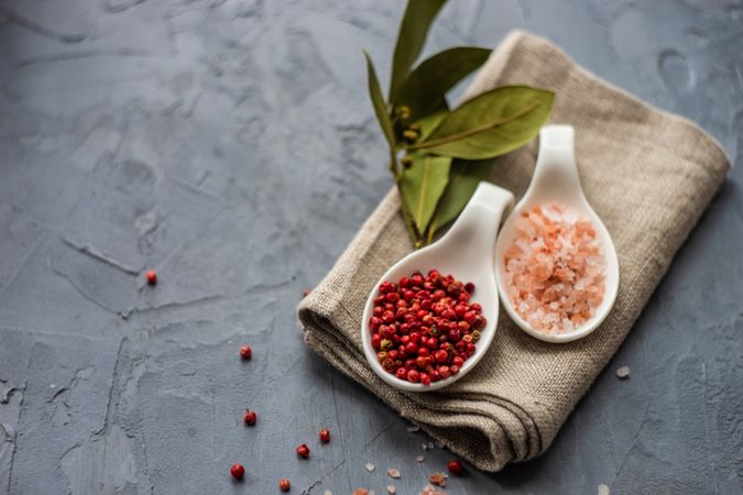 Top view of two bowls of bay leaves, Himalayan salt and red peppercorns on kitchen towel