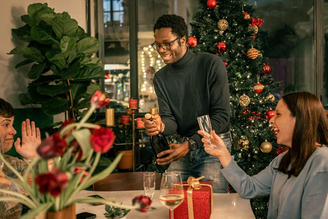 Joyful multicultural friends laughing and celebrating Christmas by opening champagne.