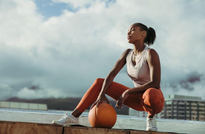 Serious woman looking away on rooftop with exercise ball