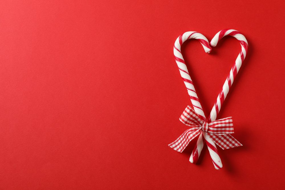 Sweet candy canes with bow on red background, space for text