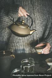 Woman in cozy sweater pouring from traditional Japanese tea set 42n8q4