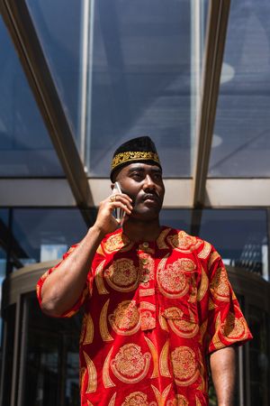Black male in traditional clothes talking on cellphone in street
