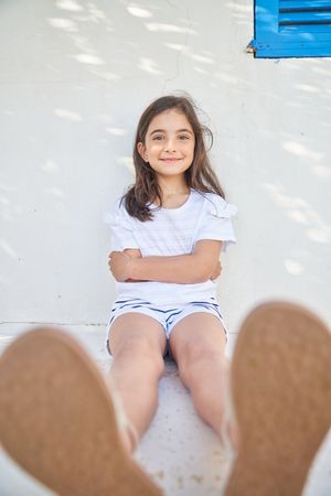 Smiling girl sitting near wall with crossed arms
