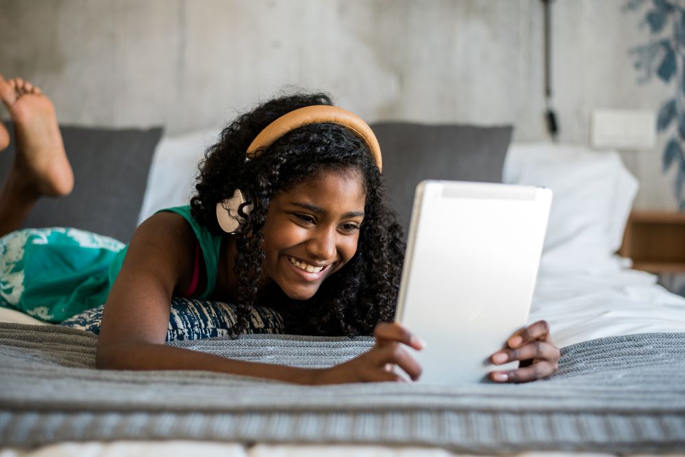 Happy young two Black women sitting and standing up in the couch on the computer and mobile phone with headphones dancing