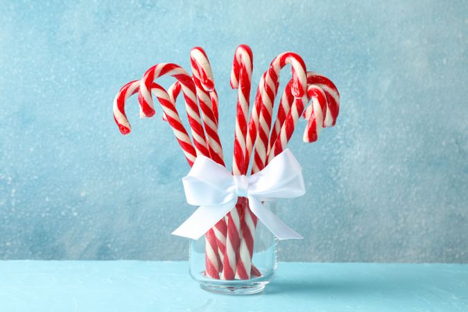 Candy canes in glass jar on blue background, space for text