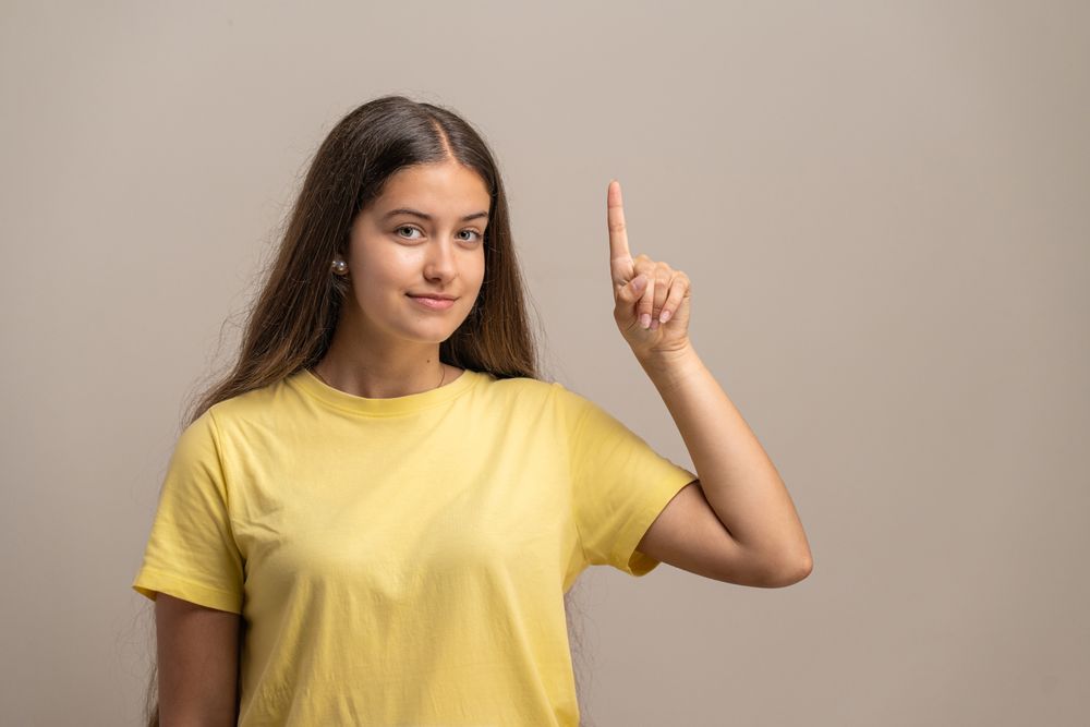 Confident young woman pointing up with her index finger for attention.