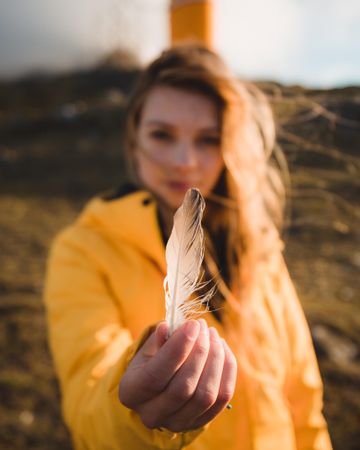 Young woman in yellow jacket holding light feather