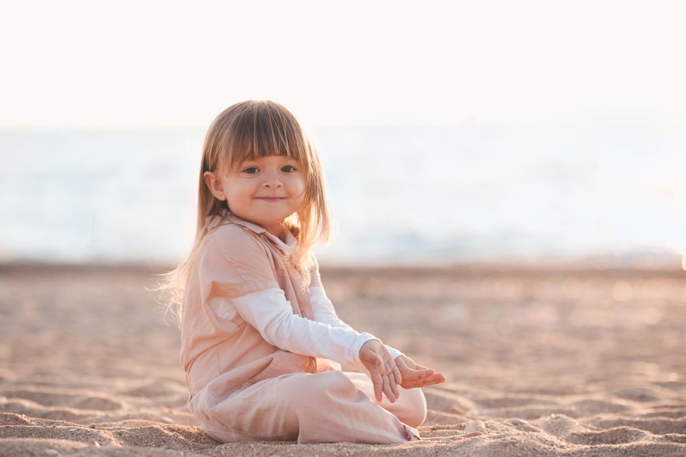 Girl in yellow outfit sitting on sandy beach