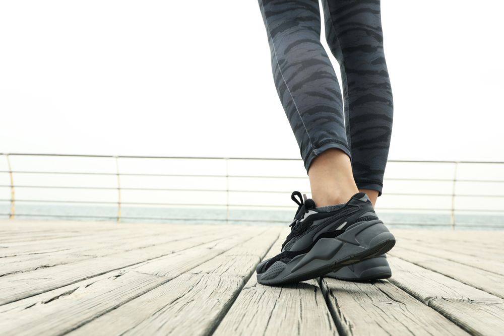 Female legs in leggings and sneakers on wooden floor outdoors, close up