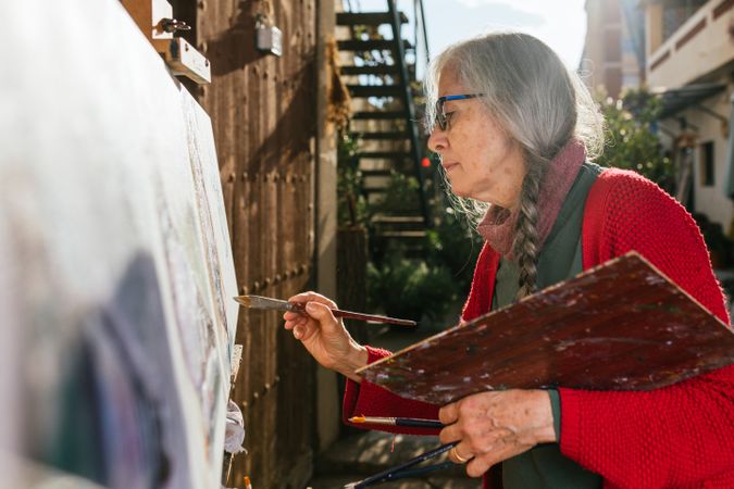 Older woman painting on canvas in garden