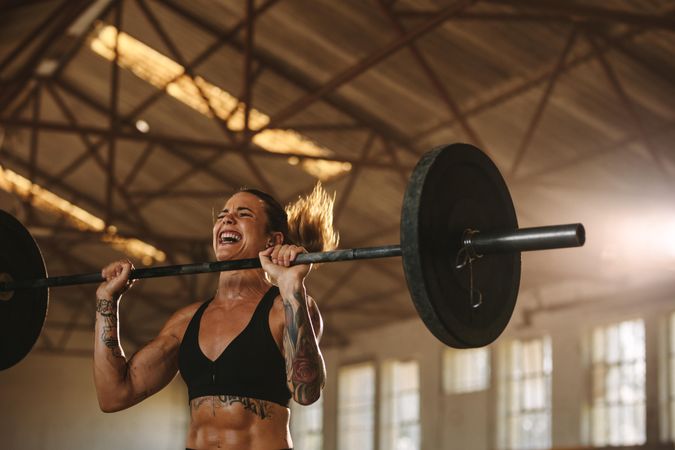 Tough young woman exercising with barbell