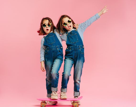 Stylish girls with skateboard and wearing fashion clothes on pink background