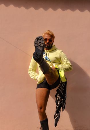 South Asian man with blonde hair wearing casual outwear kicking his left leg