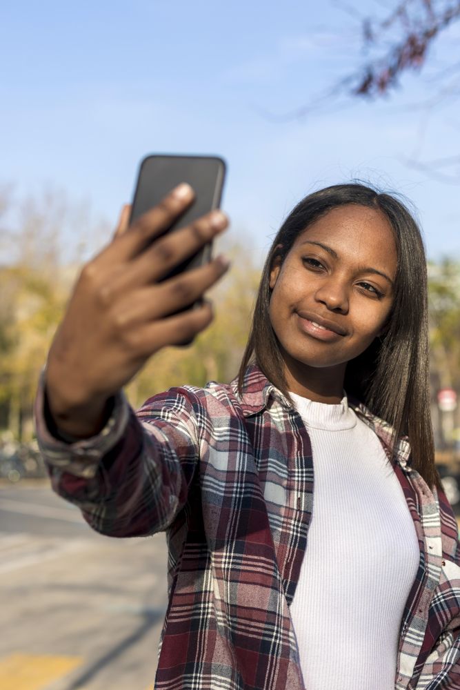 Female taking selfie with park in background, vertical