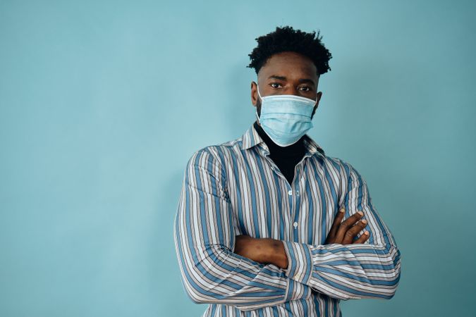 Portrait of a Black man in face mask blue striped shirt with his arms crossed