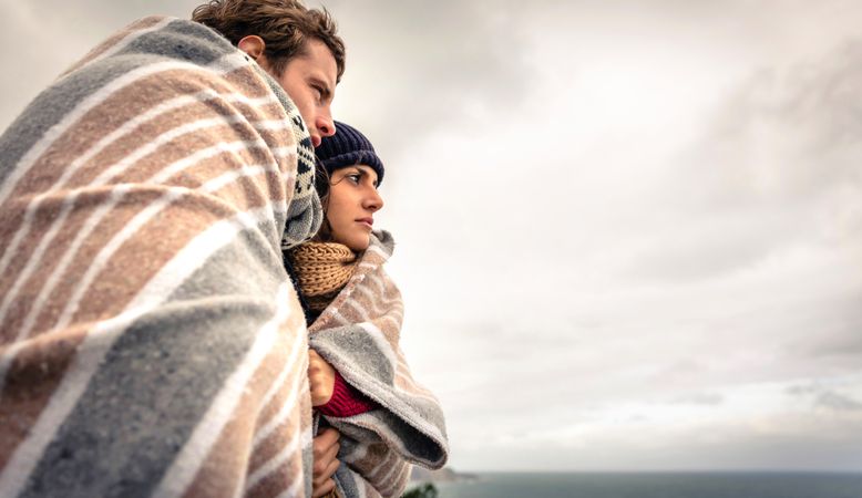 Side view of loving couple wrapped in blanket on a windy day with overcast sky