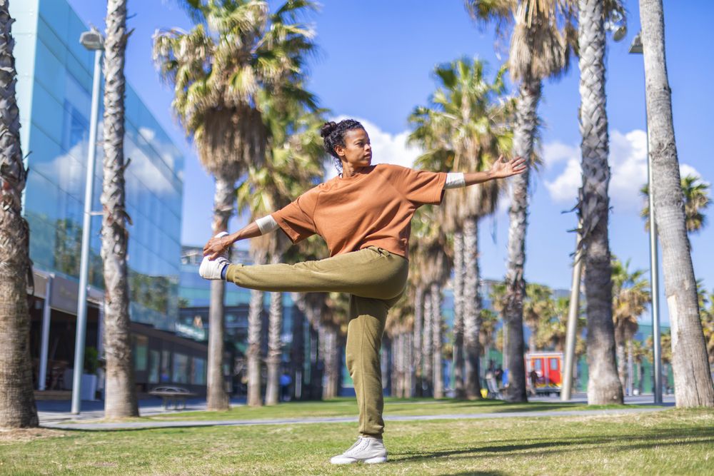 Black female stretching legs under the palms in a promenade
