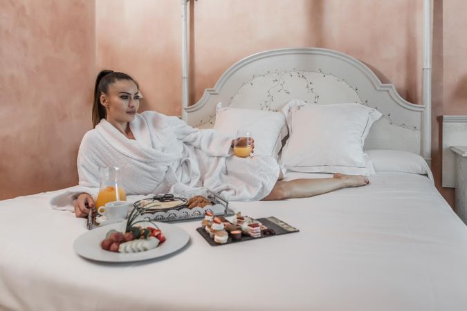 Woman with juice laying near breakfast on bed