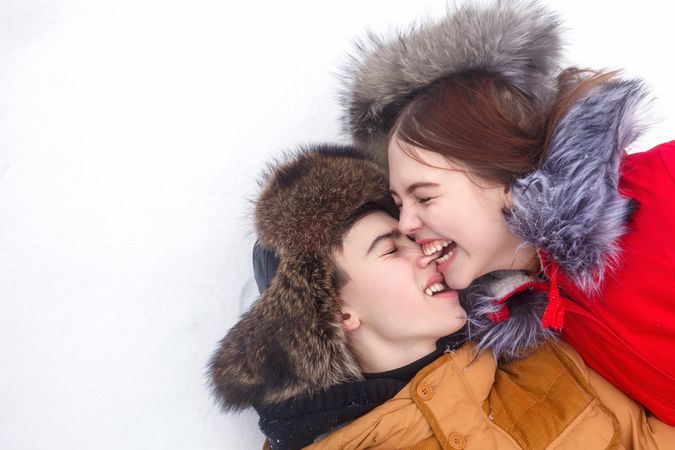 Teenage couple playfully biting each other in snow