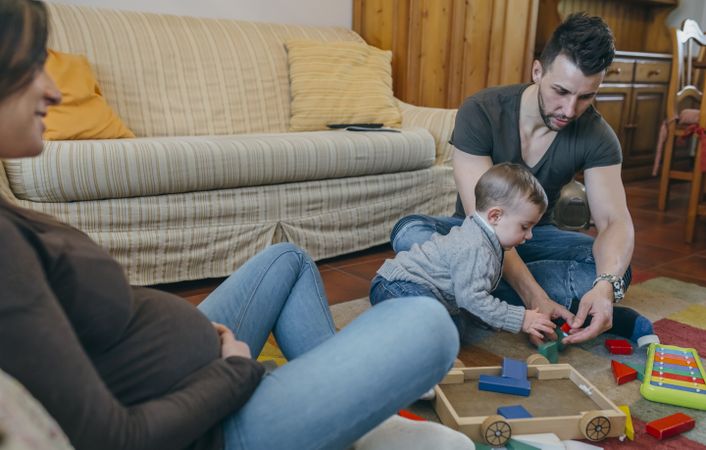 Father playing with toddler while the mother is looking at them