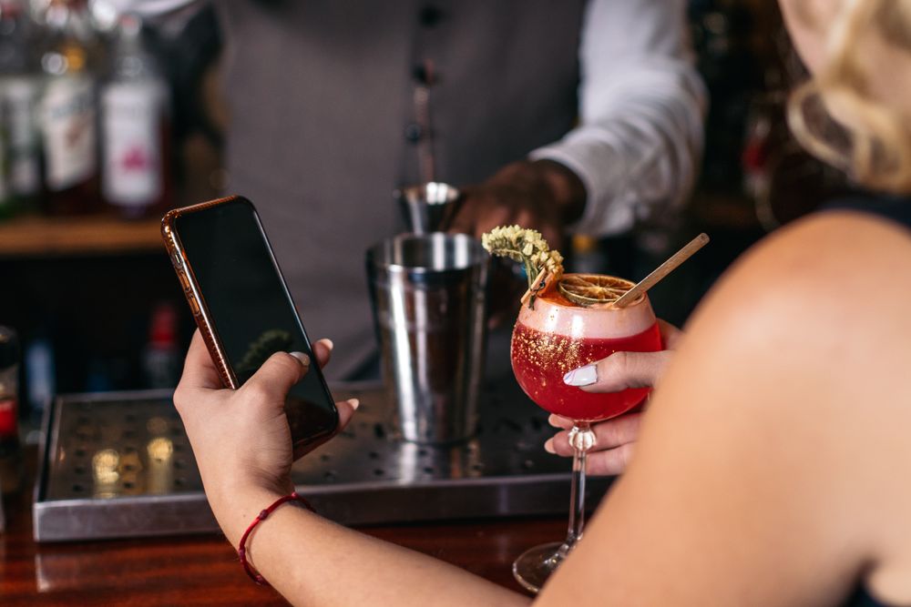 Customer having a cocktail in a traditional cocktail bar while using the smartphone