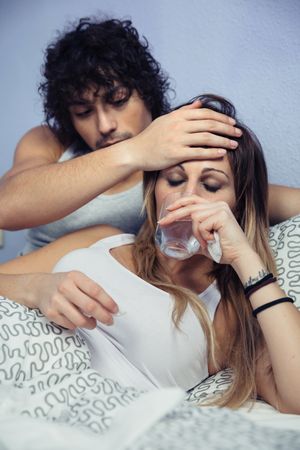 Portrait of man helping sick girlfriend drinking water in bed