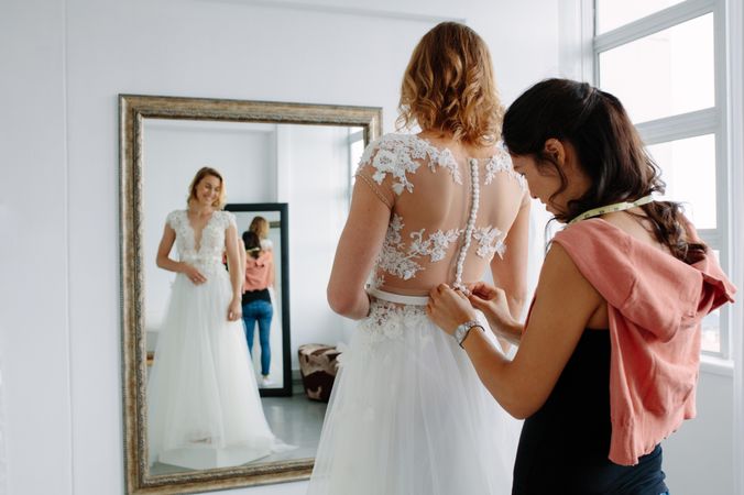 Woman assistant helping female in trying wedding dress in a shop