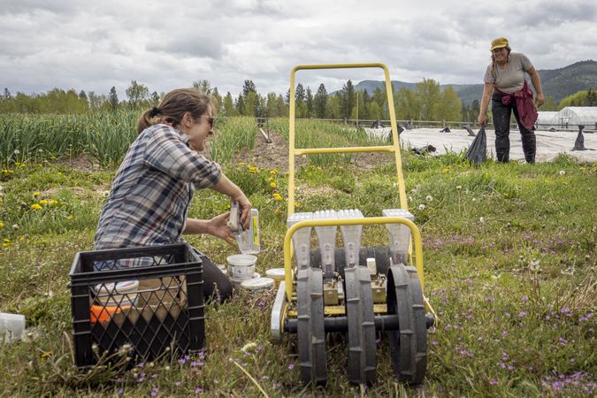 Woman with seeder on farm talking to colleague