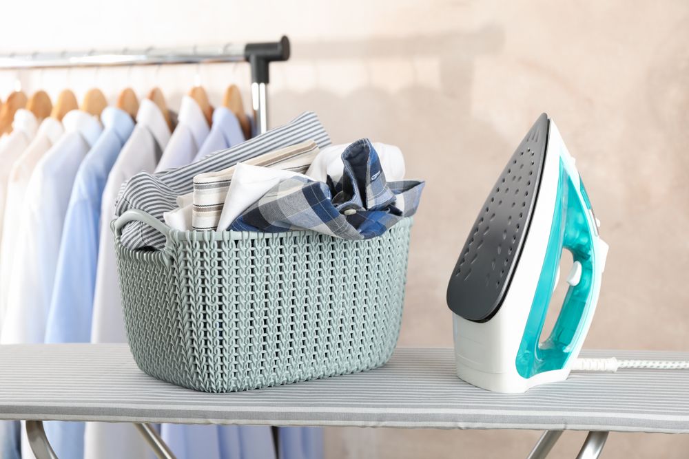 Basket with clean laundry and iron on ironing board, space for text