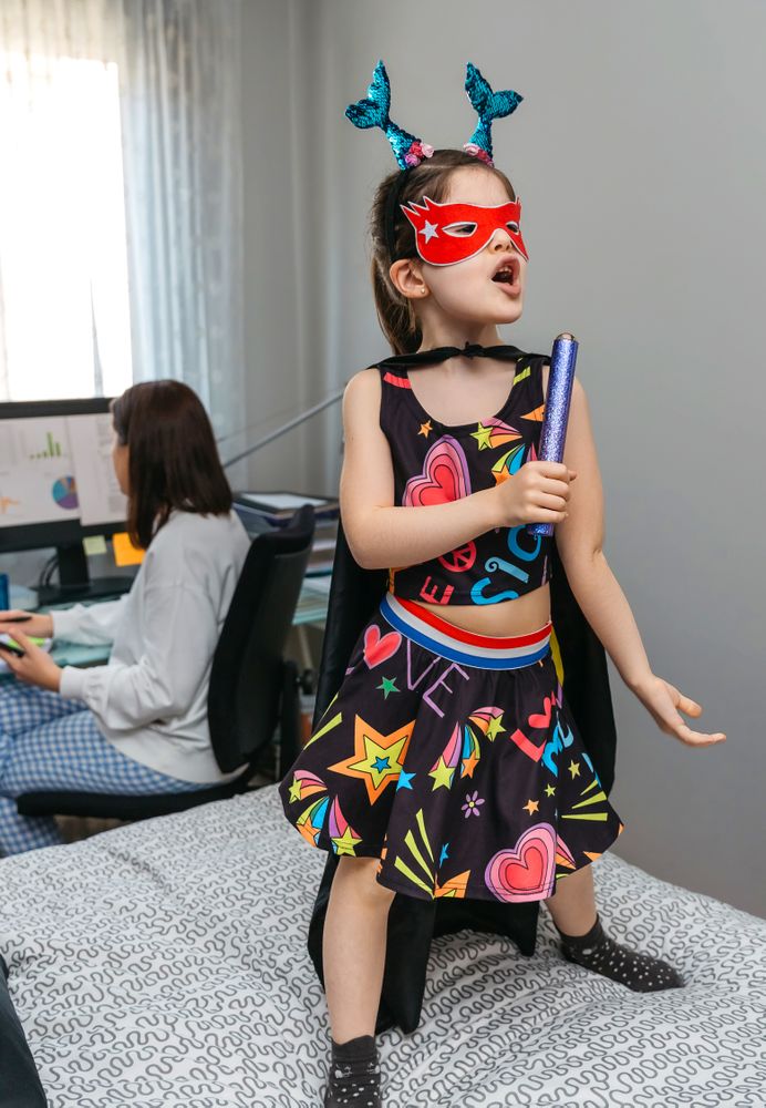 Girl in disguise singing and dancing on the bed while her mother works from home