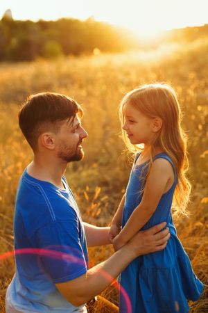 Female child hugs her father in meadow at dusk