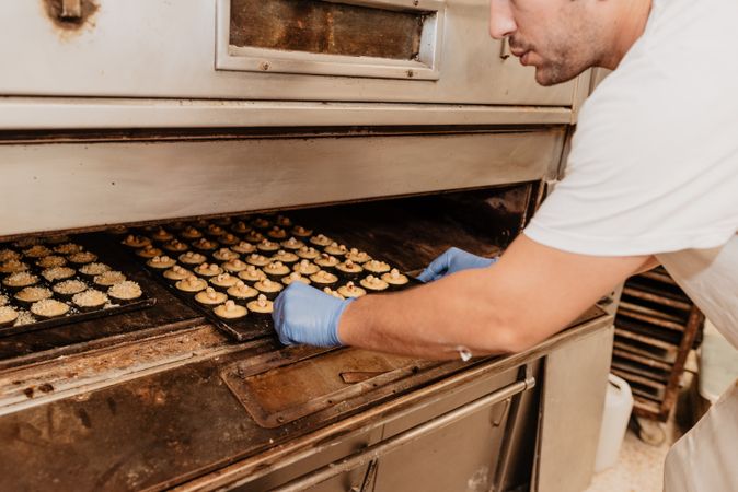 Bald baker checking pastry inside oven