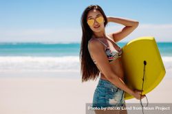 Young woman standing by the beach holding a bodyboard and looking away 4ZOZyb