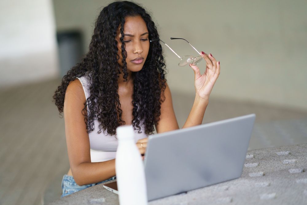 A Focused Woman Diligently Working on Her Laptop While Wearing Glasses in a Modern Workspace