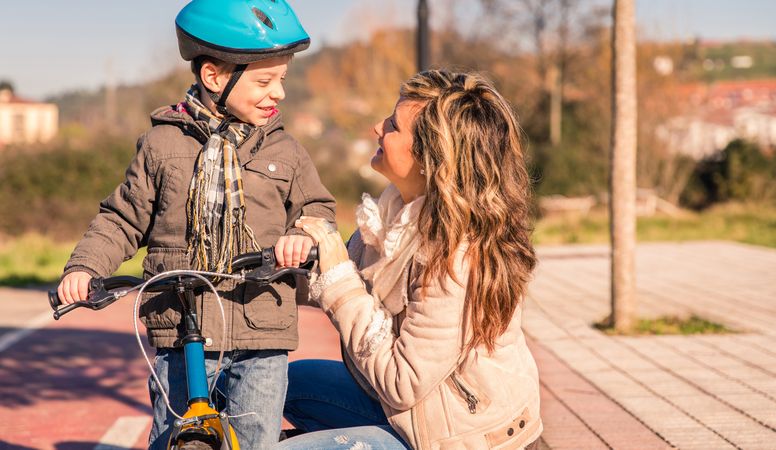 Mother smiling up at little boy on bike
