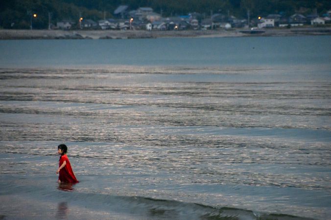 Girl in red dress wading in seashore water