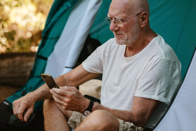 Older man sitting in tent and using his mobile phone